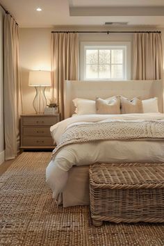 a large bed sitting under a window next to a basket filled with pillows and blankets