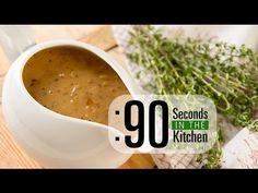 a white bowl filled with soup sitting on top of a wooden cutting board next to herbs