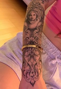 a woman's arm with tattoos on it and a gold band around her wrist