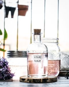 there are two bottles with liquid in them and some flowers on the table next to it