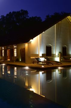 an outdoor swimming pool with chaise lounges and lights around it at night time