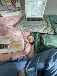 a laptop computer sitting on top of a bed next to an open book and cup