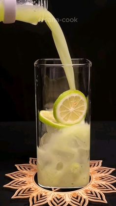 a drink being poured into a glass filled with ice and lime