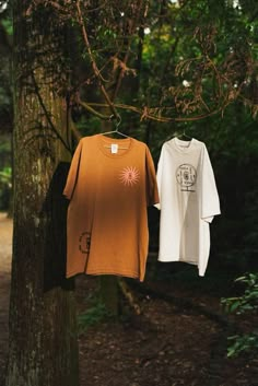 two t - shirts hanging on a clothes line in the woods, one is orange and the other is white