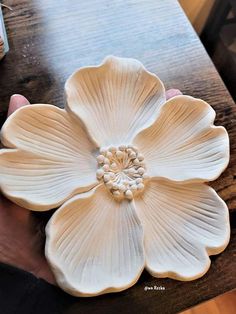 a person holding a flower shaped object on top of a wooden table in their hand