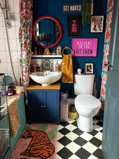 a bathroom with a checkered floor and blue walls is pictured in this image, there are pictures on the wall above the toilet