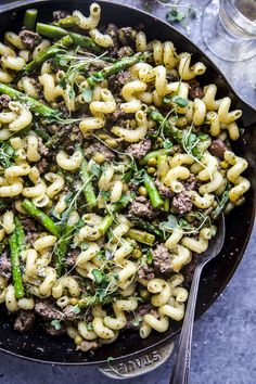 a skillet filled with pasta and asparagus on top of a gray table