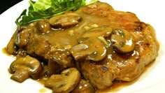 a white plate topped with meat covered in mushroom gravy and garnished with lettuce