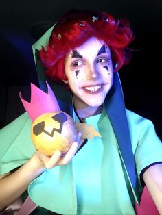 a woman with red hair and makeup holding an orange ball in her hand while wearing a costume