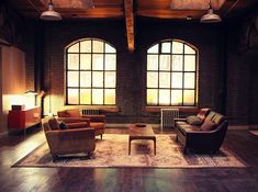 a living room filled with lots of furniture next to two large windows and a rug on the floor