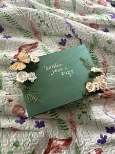 a green book with flowers on it sitting on a floral print bed spread next to a cell phone