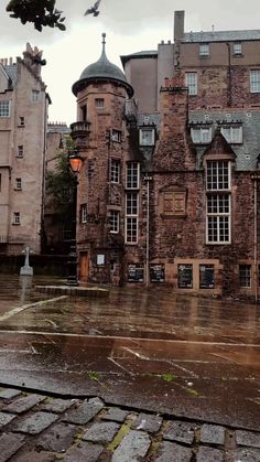 an old brick building sitting on top of a wet street next to a light pole