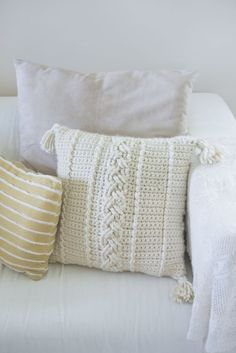 a white couch with two pillows on top of it next to a pillow and blanket