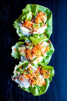 three lettuce wraps filled with shredded carrots and sauce on a blue surface