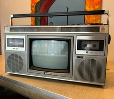 an old fashioned television sitting on top of a wooden table in front of a painting