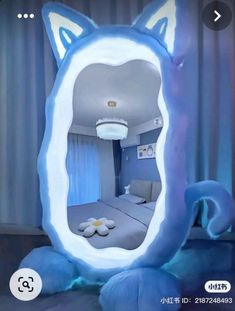 a cat shaped mirror in the shape of a bedroom with blue curtains and pillows on it