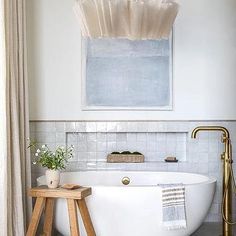 a white bath tub sitting next to a wooden stool in a bathroom under a painting