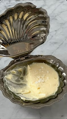 a silver bowl filled with cream sitting on top of a marble counter next to a metal spoon