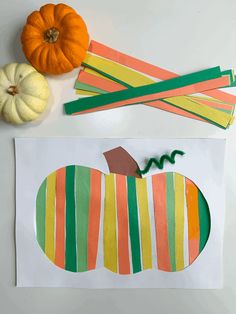 an apple cut out from strips of paper next to some pumpkins and other crafting supplies