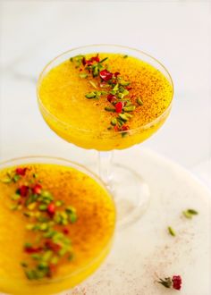 two glasses filled with yellow liquid and garnished with flowers on the rims