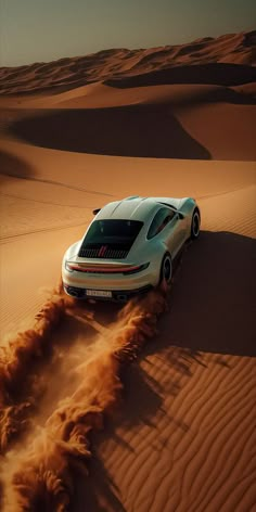 a white car driving through the desert with sand blowing in the foreground and an orange dune behind it