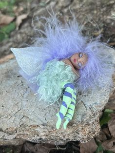 a doll is laying on a rock with blue hair and green eyeshadow,