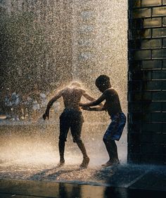 two young boys playing in the sprinkles of a fountain