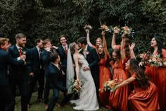 a group of people standing around each other in front of some trees and bushes with their hands up