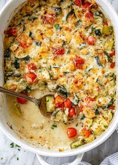 a casserole dish filled with cheese, tomatoes and zucchini on a table