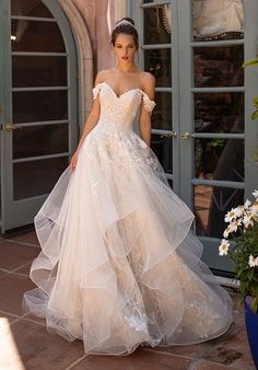 a woman in a wedding dress is standing on the sidewalk near flowers and an open door