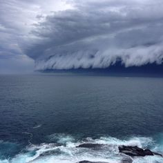 a large storm rolls in over the ocean on a cloudy day with blue water and rocks