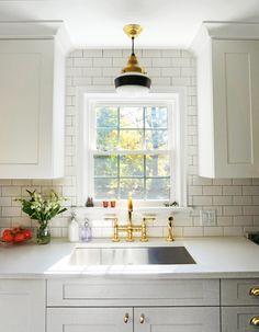 a kitchen with white cabinets and gold faucet lights above the sink, along with an open window