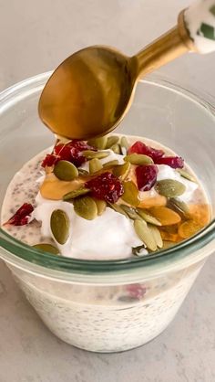 a spoon scooping yogurt into a bowl filled with fruit and nuts on top