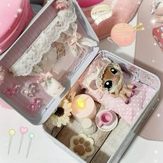 a small doll in a pink box on a table with other dolls and decorations around it