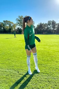 a girl in green soccer uniform standing on the field with her hands behind her back