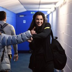 two people walking down a hallway with backpacks on their backs and one person giving the thumbs up