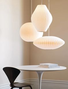 three white lamps hanging from the ceiling above a table with two chairs in front of it