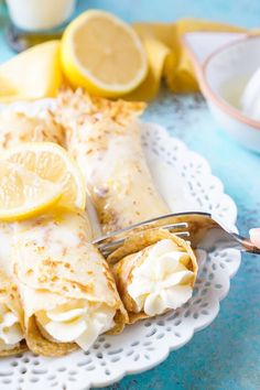 a white plate topped with crepes covered in icing and lemon wedges