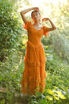 a woman in an orange dress is standing in the grass with her hands behind her head