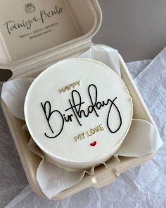 a birthday cake with the words happy birthday in black writing on it sitting in a box