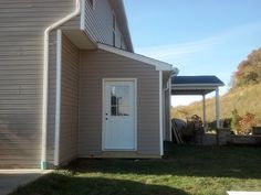 a gray house with a white door on the side and grass in front of it