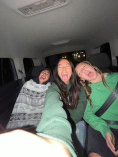 three people sitting in the back of a car with their mouths open and one person taking a selfie