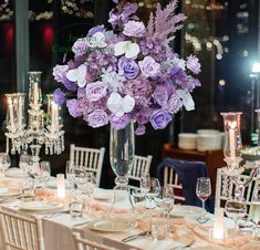 a vase filled with purple and white flowers sitting on top of a table covered in candles