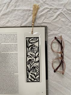 an open book next to some glasses on a white sheet with a black and white pattern