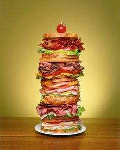 a large stack of sandwiches sitting on top of a white plate next to a red apple