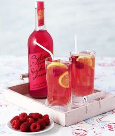 two glasses filled with raspberry lemonade next to a bottle of booze