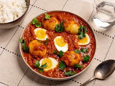 a bowl filled with meat and eggs on top of a table next to some rice