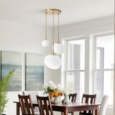 the dining room table is surrounded by chairs and vases with flowers on them in front of two large windows