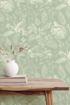 a white vase with some plants in it on a table next to a wall paper