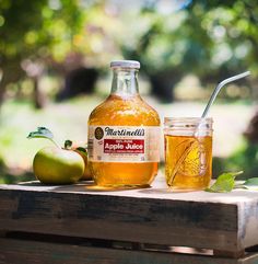 an apple cider and two apples on a wooden table